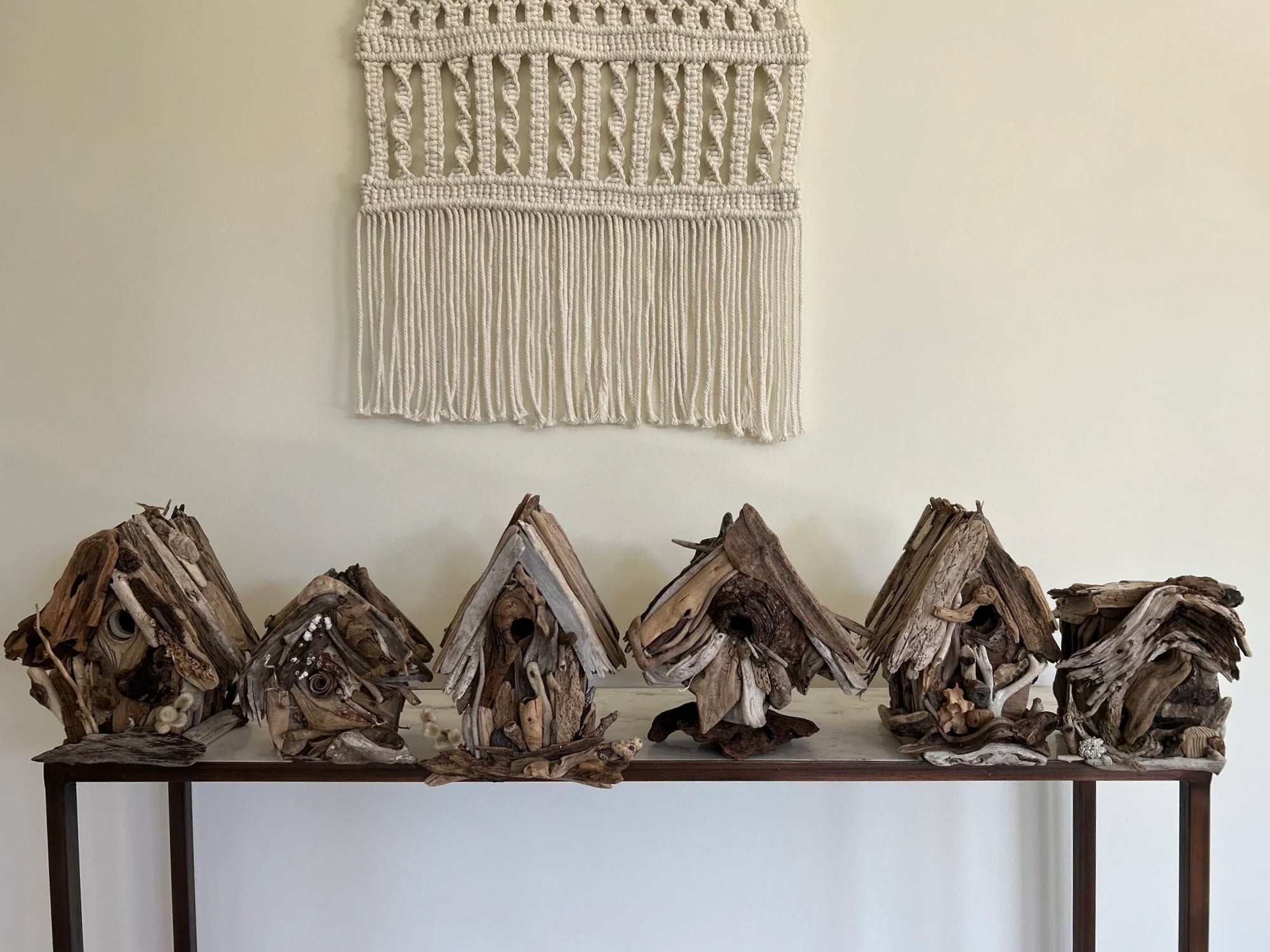 Six driftwood birdhouses in a row on a marble table